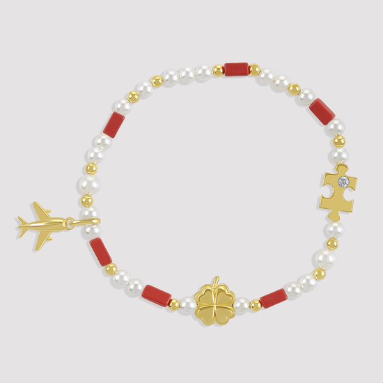 Bracelet with pearls, red beads, gold airplane, clover, and puzzle piece charms on a light gray background