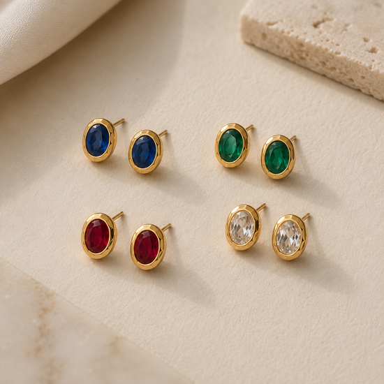 Set of gold earrings with colored gemstones on a beige surface