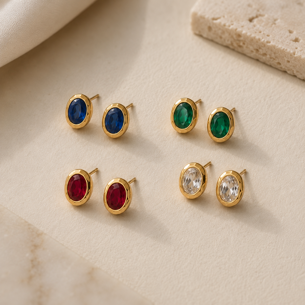 Set of gold earrings with colored gemstones on a beige surface