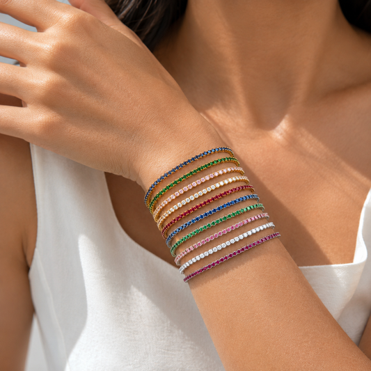Close-up of a person's arm wearing multiple colorful tennis bracelets on a neutral background