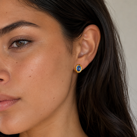 Close-up of a woman wearing a gold earring with a blue gemstone.