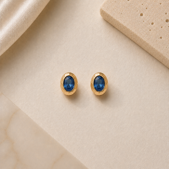 Gold earrings with blue gemstones on a beige surface