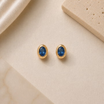 Gold earrings with blue gemstones on a beige surface