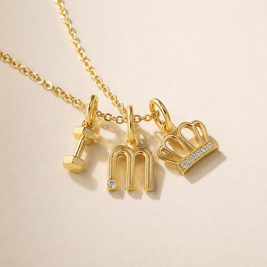Gold necklace with three charms on a beige background