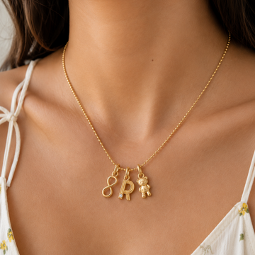 Gold necklace with letter charms worn by a person in a white top with floral details.
