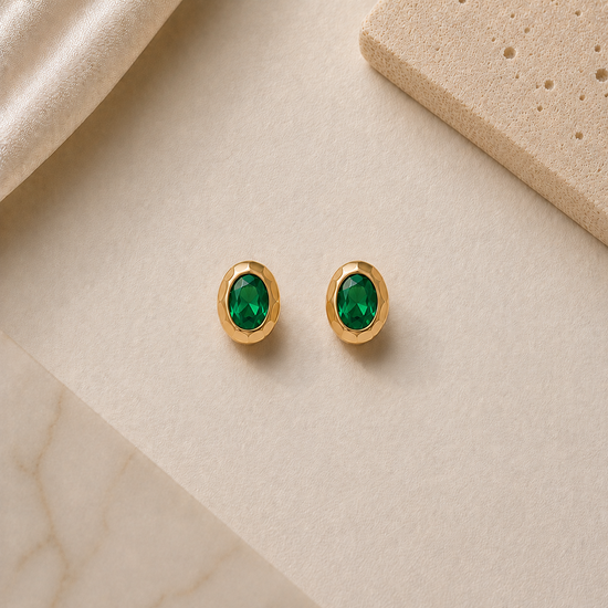 Gold earrings with green gemstones on a beige surface