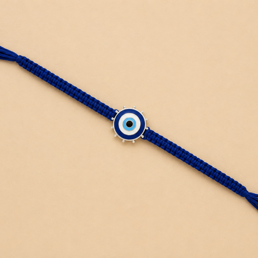 A blue braided cord bracelet with a central evil eye charm, displayed diagonally on a solid beige background.