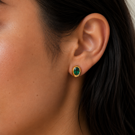 Close-up of an ear wearing a gold earring with a green gemstone.