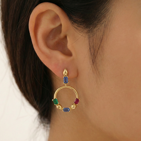 Gold hoop earring with colorful gemstones worn by a person.