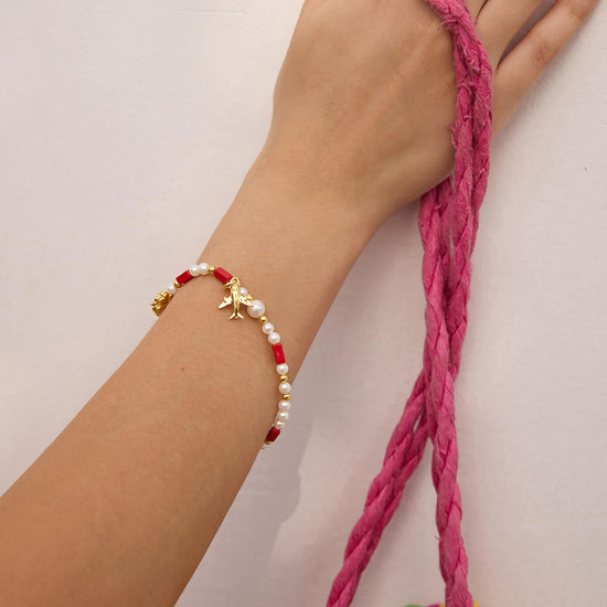 Bracelet with red and gold beads on a wrist against a neutral background
