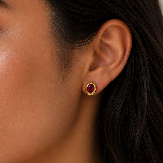 Close-up of an ear wearing a gold earring with a red gemstone.