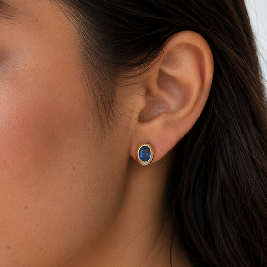 Close-up of an ear wearing a gold earring with a blue gemstone.