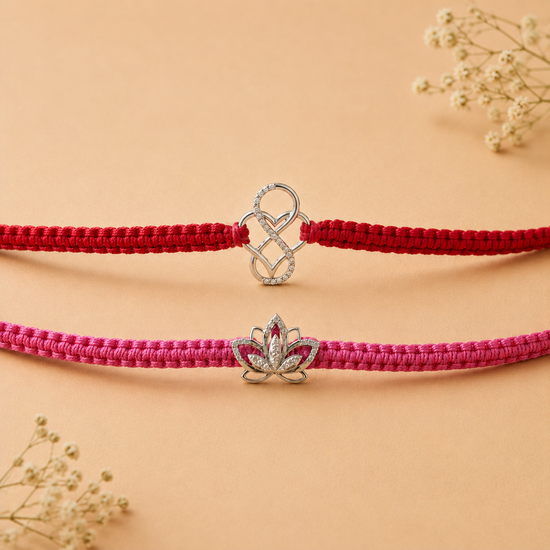 Two braided cord bracelets, one red and one pink, each featuring a silver-toned charm. The top bracelet has a silver heart-and-loop charm, while the bottom bracelet has a silver lotus flower charm with a small red gemstone in the center.