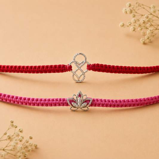 Two braided cord bracelets, one red and one pink, each featuring a silver-toned charm. The top bracelet has a silver heart-and-loop charm, while the bottom bracelet has a silver lotus flower charm with a small red gemstone in the center.