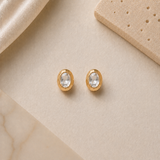 Gold earrings with clear gemstones on a beige surface