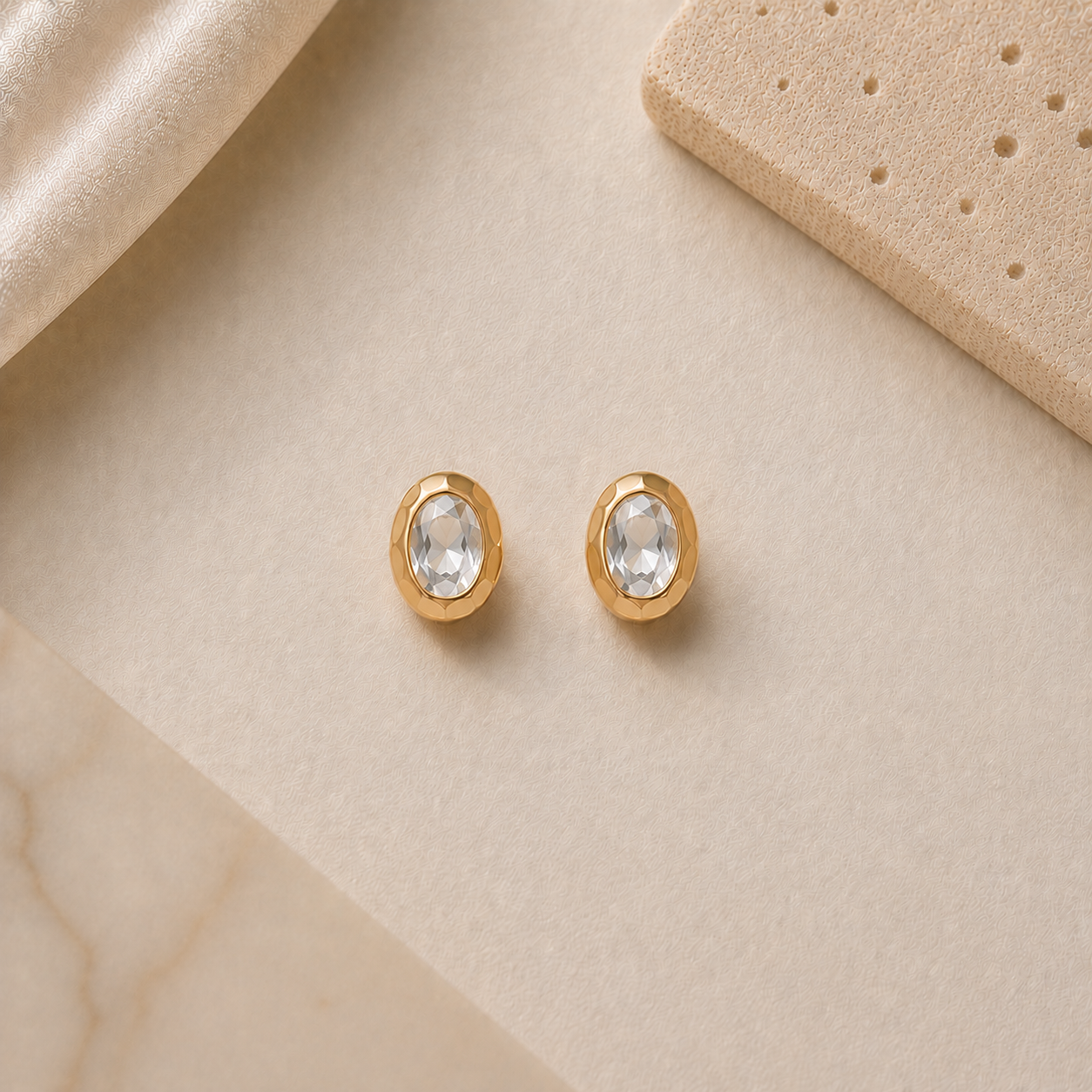 Gold earrings with clear gemstones on a beige surface