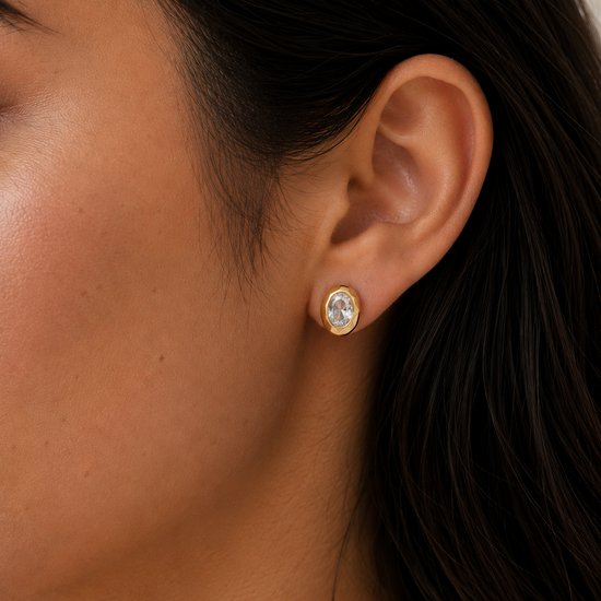 Close-up of an ear wearing a gold earring with a clear gemstone.