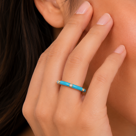 Close-up of a hand wearing a turquoise ring with gold accents, touching the cheek.