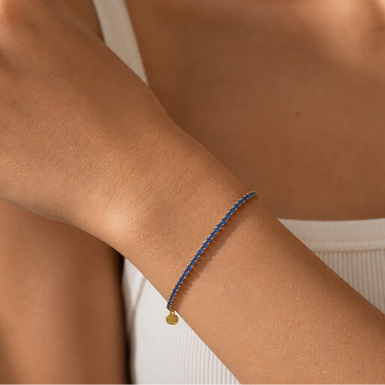 Close-up of a wrist wearing a blue beaded bracelet with a gold charm.