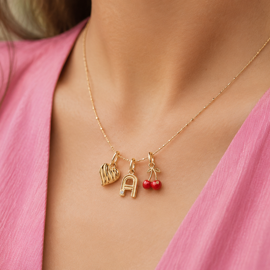 Gold necklace with charms on a person wearing a pink top