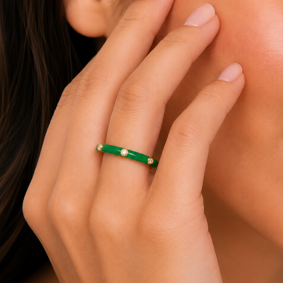 Close-up of a hand wearing a green ring with small pearls on a blurred background