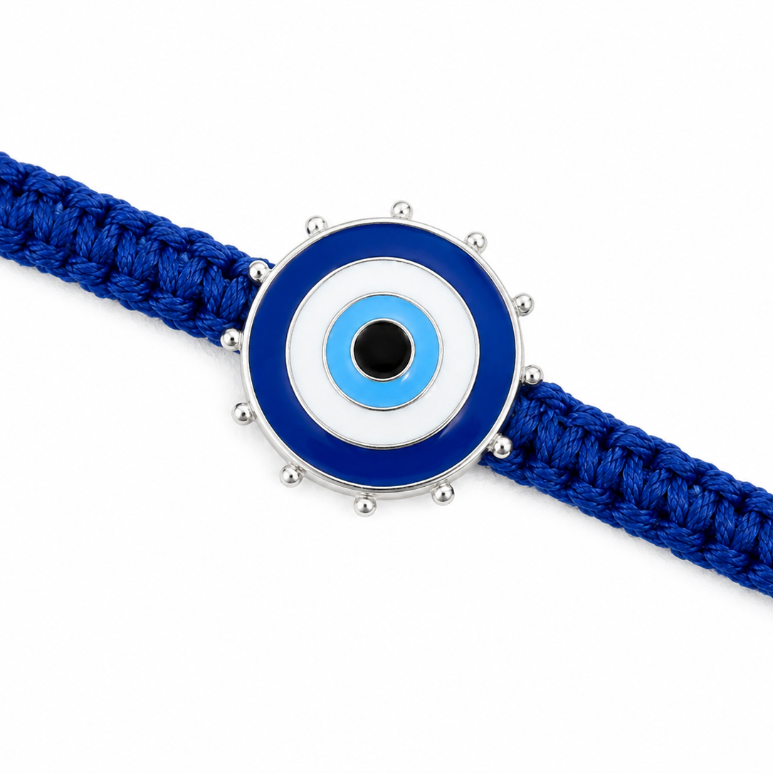 A blue braided cord bracelet featuring a circular evil eye charm with blue, white, and black enamel details and silver-tone metal accents, shown on a plain white background.