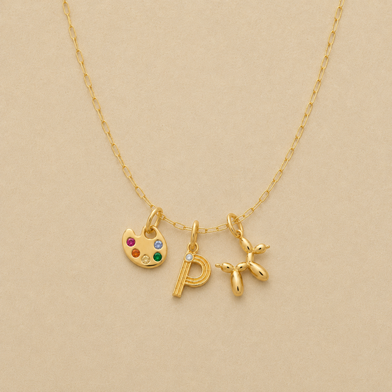 Gold necklace with a paint palette, letter 'P', and star pendant on a beige background