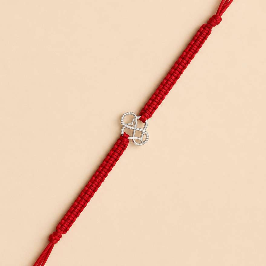 A red braided cord bracelet with a silver infinity symbol charm set with small clear stones, displayed diagonally on a solid beige background.
