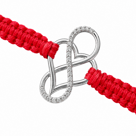 A close-up of a red braided cord bracelet with a silver infinity-style heart charm set with small clear stones, on a plain white background.