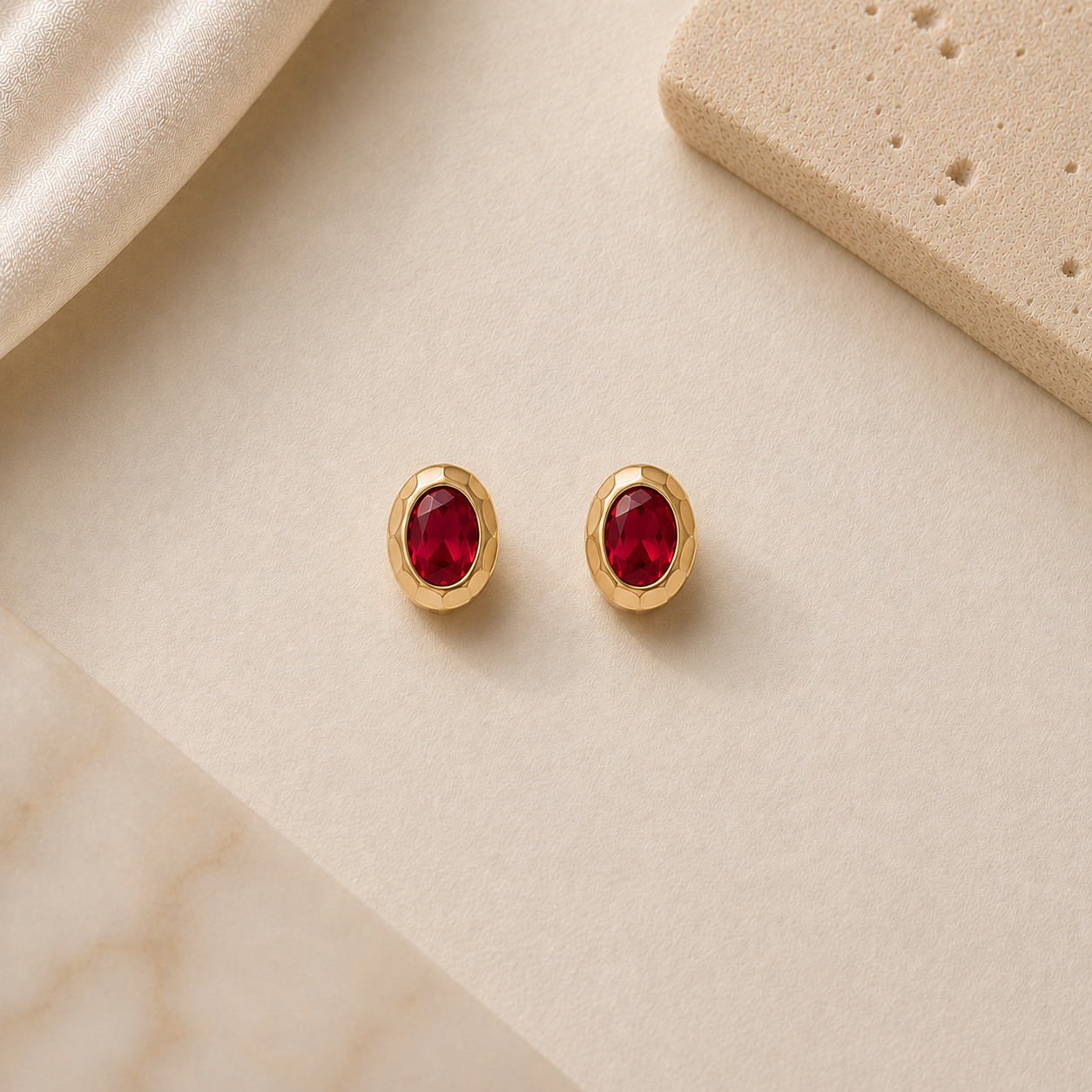 Gold earrings with red gemstones on a beige fabric background