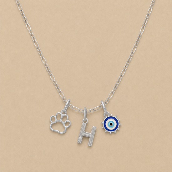 Silver necklace with paw print, letter 'H', and evil eye charm on a beige background