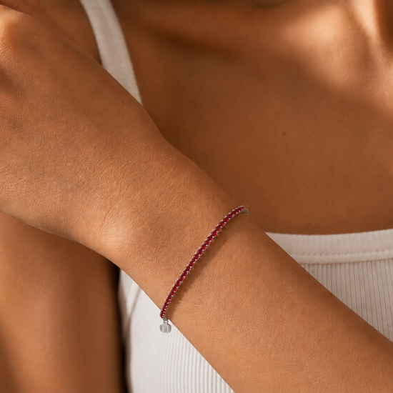 Close-up of a person's arm wearing a red beaded bracelet on a neutral background