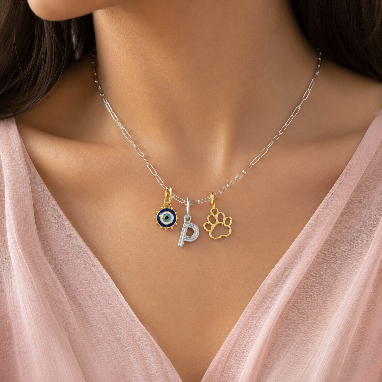 Necklace with charms including a paw print, letter 'P', and evil eye on a model wearing a pink top.