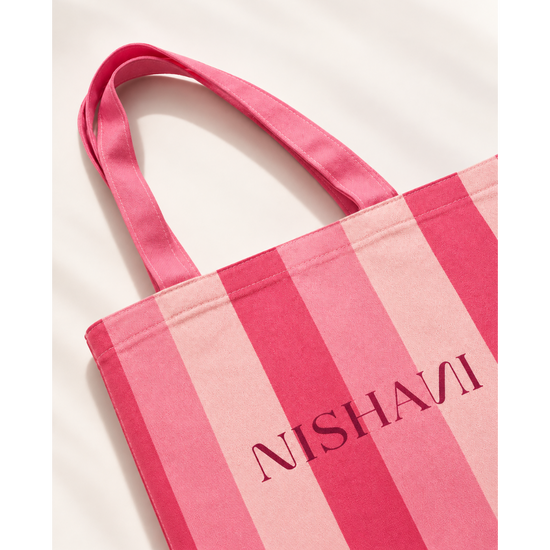 A pink striped canvas tote bag with the brand name 'NISHANI' printed in dark pink lettering, shown on a clean white background.
