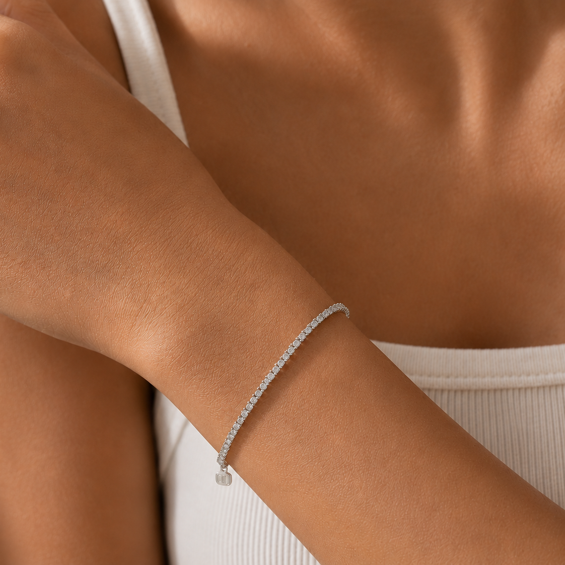 Close-up of a person's arm wearing a delicate silver bracelet against a neutral background